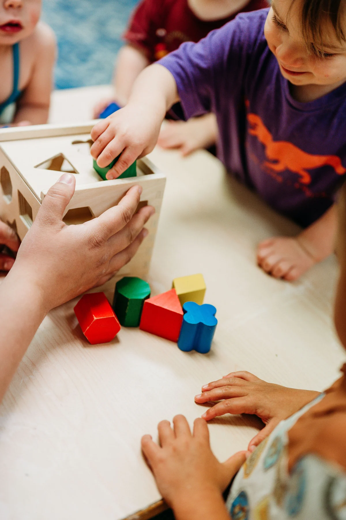 Children exploring a wooden shape sorter with a Kindred Hill guide