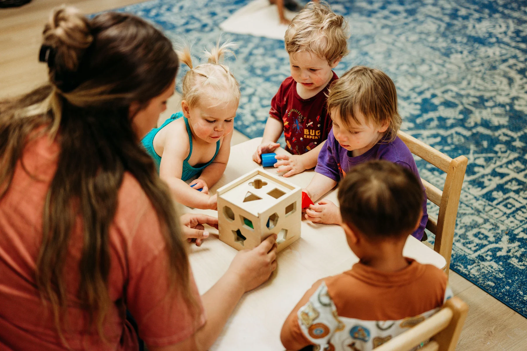 Young children exploring a shape sorter together with a guide at Kindred Hill